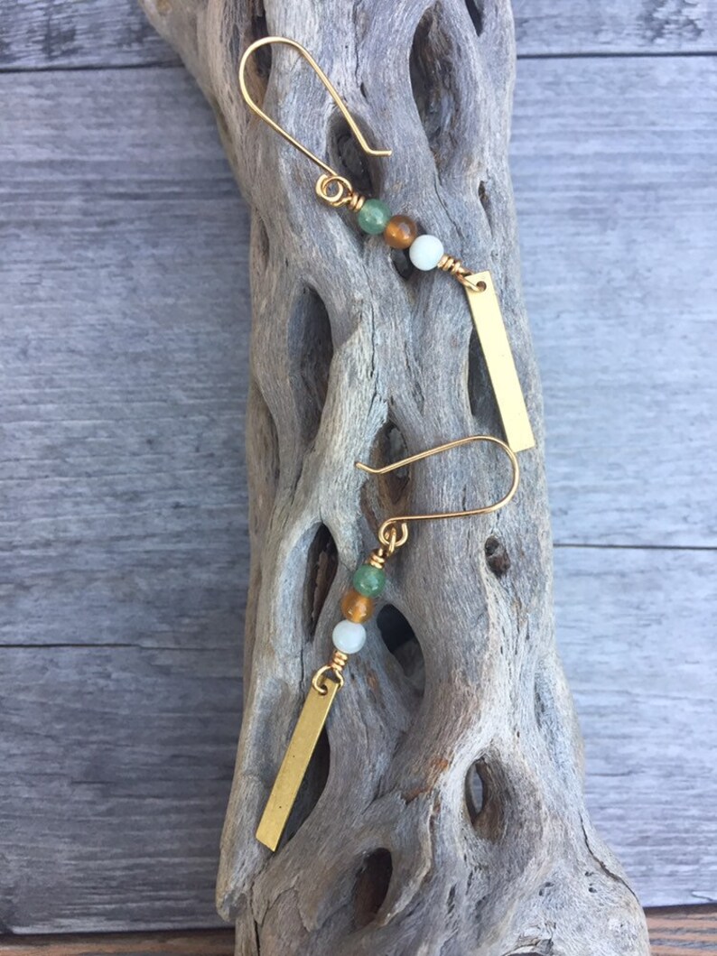 May include: Gold earrings with a small gold bar charm and three beads: green, brown, and white.