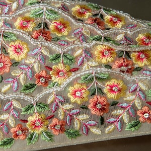 May include: A close-up of a beige lace trim with embroidered flowers in shades of yellow, orange, pink, and green.
