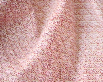 May include: Close-up of a fabric with a repeating floral pattern. The design features small, stylized flowers in a deep red color against a cream-colored background. The fabric is slightly wrinkled, suggesting it is soft and pliable.
