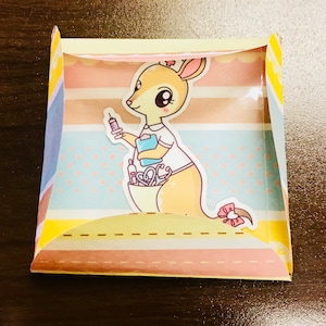 May include: A yellow and pink card featuring a cartoon kangaroo dressed as a nurse, holding a syringe. The kangaroo is surrounded by medical supplies, including a stethoscope and a bandage. The card has a white background with pink and blue stripes.