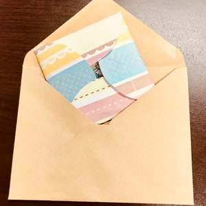 May include: A brown paper envelope with a colourful patterned card inside. The card has stripes, polka dots, and scalloped edges.