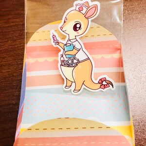 May include: A cute cartoon kangaroo wearing a nurse's uniform and a red cross hat. The kangaroo is holding a syringe and has a stethoscope and other medical supplies in its pouch. The image is on a colourful background with stripes and polka dots.