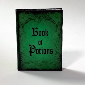 Pu&ograve; includere: Un piccolo libro rettangolare con una copertina verde e testo nero che dice "Book of Potions". La copertina ha un bordo decorativo e un aspetto invecchiato. Il libro &egrave; in piedi.