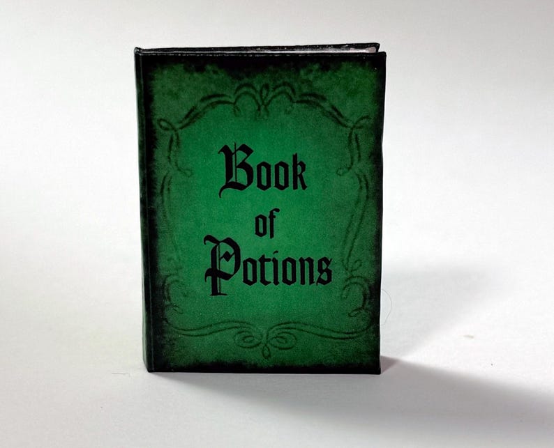 Pu&ograve; includere: Un piccolo libro rettangolare con una copertina verde e testo nero che dice "Book of Potions". La copertina ha un bordo decorativo e un aspetto invecchiato. Il libro &egrave; in piedi.