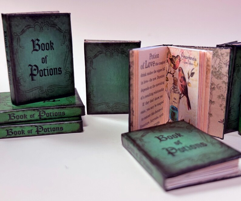 Pu&ograve; includere: Miniature libri verdi "Book of Potions" con copertine invecchiate e strutturate. Un libro &egrave; aperto, rivelando pagine illustrate con testo e un disegno di un uccello e una bottiglia di pozione. I libri sono impilati e disposti su una superficie bianca.