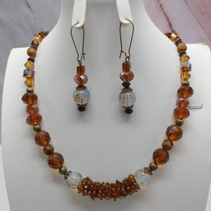 May include: A brown and clear glass beaded necklace and matching earrings. The necklace has a center piece of white glass beads with gold accents.