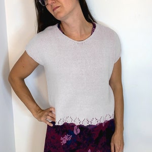 May include: A white knitted top with a scalloped hem and short sleeves. The top is worn over a floral print skirt.