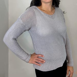 May include: A light gray knit sweater with long sleeves and a scoop neck. The sweater has a textured appearance and is worn by a person. The person is smiling and has dark hair.