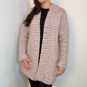 May include: A long-sleeved, light pink crocheted cardigan with a textured stitch pattern. The cardigan has a V-neck and is open in the front.