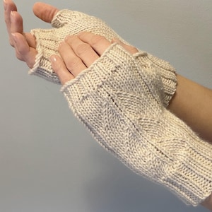 May include: A pair of cream-colored fingerless gloves. The gloves are knitted with a textured pattern and have a ribbed cuff. The open-finger design allows for dexterity while keeping the hands warm. The gloves are made of a soft, warm material.