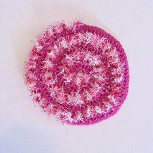 May include: A pink and white crocheted round dishcloth with a fluffy texture.