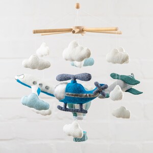 May include: A baby mobile with a blue helicopter, a white airplane, and white clouds. The mobile is made of felt and has a wooden frame.