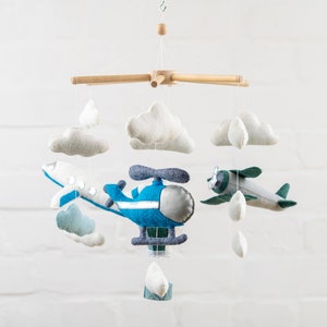 May include: A wooden mobile with blue and green felt airplanes, a blue felt helicopter, and white felt clouds. The mobile is hanging from a white ceiling.
