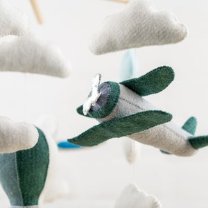 May include: A mobile with a gray and green airplane, a hot air balloon, and white clouds. The airplane has a silver propeller.