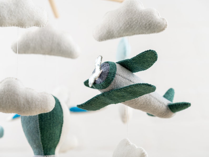 May include: A mobile with a gray and green airplane, a hot air balloon, and white clouds. The airplane has a silver propeller.