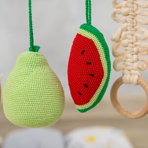 May include: A crocheted baby toy set with a green pear, a red watermelon, a wooden ring, and a white macrame ring.