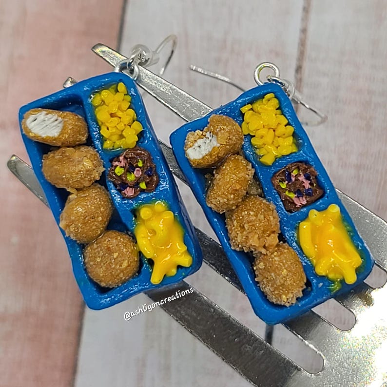 May include: A pair of blue tray earrings with a miniature depiction of a school lunch tray. The tray contains chicken nuggets, corn, mac and cheese, and a side of fruit. The earrings are made of polymer clay and have silver hooks.