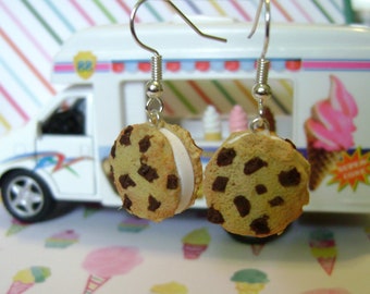 May include: A pair of dangle earrings featuring a chocolate chip cookie with a white frosting filling. The earrings are hanging from silver hooks.