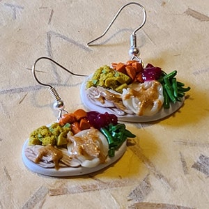 May include: A pair of earrings shaped like a plate of Thanksgiving dinner. The earrings are made of polymer clay and feature a turkey, stuffing, mashed potatoes, gravy, cranberry sauce, green beans, and carrots.