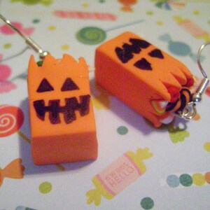 May include: A pair of orange and black Halloween-themed earrings featuring a jack-o'-lantern design. The earrings are made of polymer clay and have silver hooks.