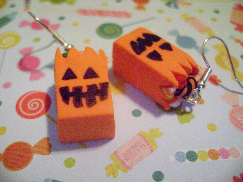 May include: A pair of orange and black Halloween-themed earrings featuring a jack-o'-lantern design. The earrings are made of polymer clay and have silver hooks.
