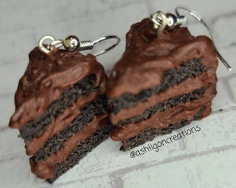 May include: A pair of chocolate cake slice earrings with chocolate frosting. The earrings are made of polymer clay and have silver hooks.