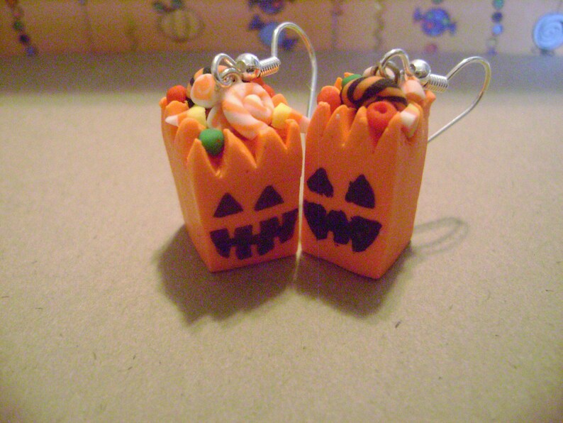 May include: A pair of orange pumpkin-shaped earrings with candy inside. The earrings are made of polymer clay and have a black jack-o'-lantern face.