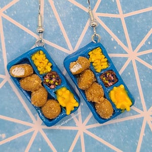 May include: A pair of blue and white earrings shaped like a miniature plastic tray of chicken nuggets, corn, and mac and cheese. The earrings are made of polymer clay and have silver hooks.