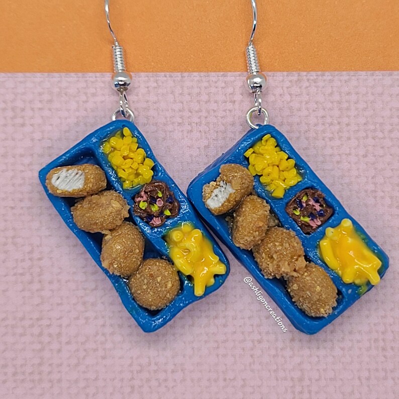 May include: A pair of blue tray earrings with a miniature depiction of a school lunch. The tray contains chicken nuggets, corn, mac and cheese, and a brownie.