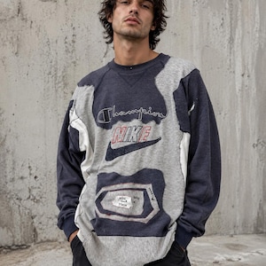 Könnte beinhalten: Ein langärmeliges Sweatshirt mit Rundhalsausschnitt, das aus Patchwork-Einsätzen aus grauem und marineblauem Stoff gefertigt ist. Die Vorderseite zeigt gestickte Champion- und Nike-Logos sowie einen kleinen weißen Aufnäher mit dem Text HIDE YOUR STASH.