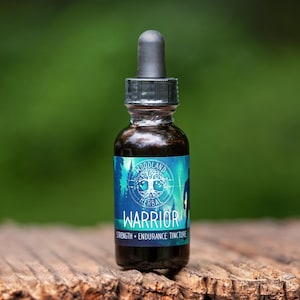 Puede incluir: Una pequeña botella de vidrio oscuro con un tapón cuentagotas negro. La botella tiene una etiqueta azul y blanca con las palabras "Warrior Strength + Endurance Tincture" y un gráfico de árbol. La botella está sobre una superficie de madera desgastada sobre un fondo verde borroso.