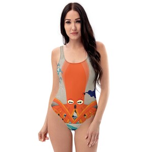 Puede incluir: Un traje de baño de una pieza con una ilustración colorida de un pulpo con una expresión de sorpresa. El pulpo está rodeado de olas y nubes. El traje de baño es de color gris claro con un escote redondo y espalda de nadador.