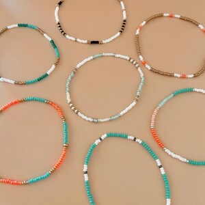Peut inclure: Plusieurs bracelets de perles de diff&eacute;rentes couleurs. Les bracelets sont compos&eacute;s de petites perles color&eacute;es blanches, noires, dor&eacute;es, oranges, turquoise et vertes. Les bracelets sont dispos&eacute;s en cercle sur un fond neutre.