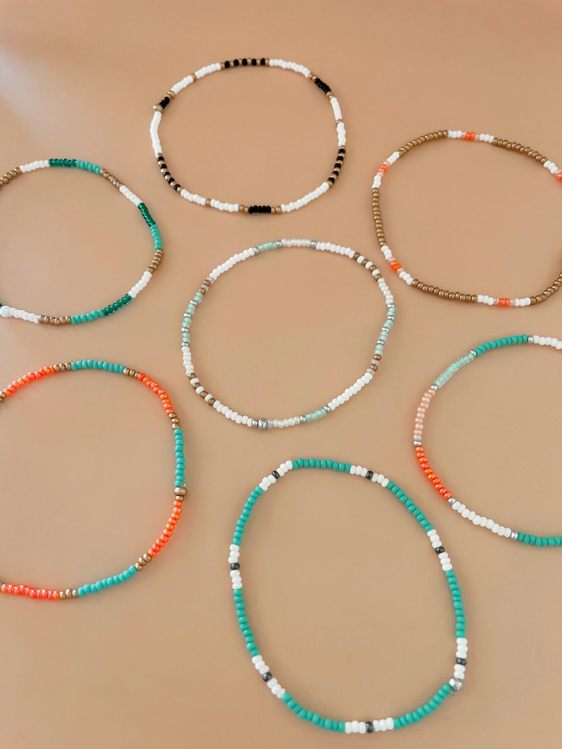 Peut inclure: Plusieurs bracelets de perles de diff&eacute;rentes couleurs. Les bracelets sont compos&eacute;s de petites perles color&eacute;es blanches, noires, dor&eacute;es, oranges, turquoise et vertes. Les bracelets sont dispos&eacute;s en cercle sur un fond neutre.