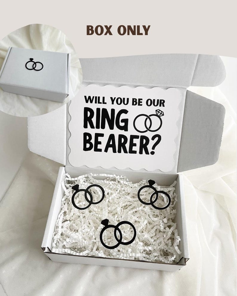 May include: A white cardboard gift box with the text BOX ONLY at the top. The inside lid features the text WILL YOU BE OUR RING BEARER? with a diamond ring icon. The box contains white paper filler and three black diamond ring cutouts.