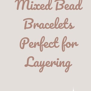 Peut inclure: Bracelets de perles mixtes de diff&eacute;rentes couleurs, dont blanc, turquoise, orange et or. Les bracelets sont pr&eacute;sent&eacute;s sur un poignet et un tissu roul&eacute;. Le texte "Mixed Bead Bracelets Perfect for Layering" est inclus.