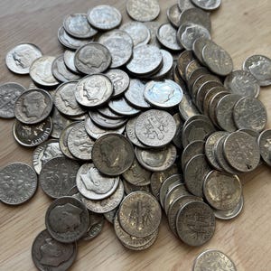 May include: A large pile of silver-colored US dimes, featuring the profile of Franklin D. Roosevelt on one side and a bundle of wheat stalks on the other.