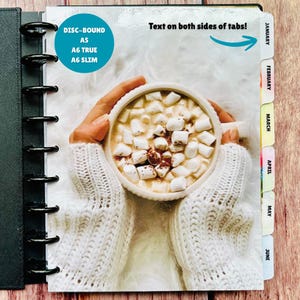 May include: A disc-bound planner featuring a cover image of a mug filled with marshmallows. The text reads DISC-BOUND A5, A6 TRUE, A6 SLIM, and Text on both sides of tabs. The side tabs are labeled January through June in black text.
