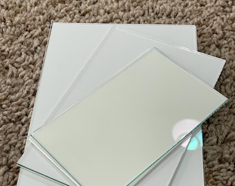 May include: A stack of square, white glass tiles with beveled edges. The tiles are arranged in a layered pattern, with the top tile slightly offset. The glass reflects light, creating highlights and shadows.