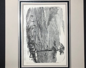 May include: Black and white framed print of a landscape scene with text. The print depicts a detailed illustration of a river, trees, and structures. The print is matted and framed in a black and silver frame.