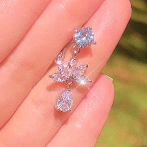 May include: A silver dangle earring with a clear crystal flower and a teardrop-shaped crystal pendant.