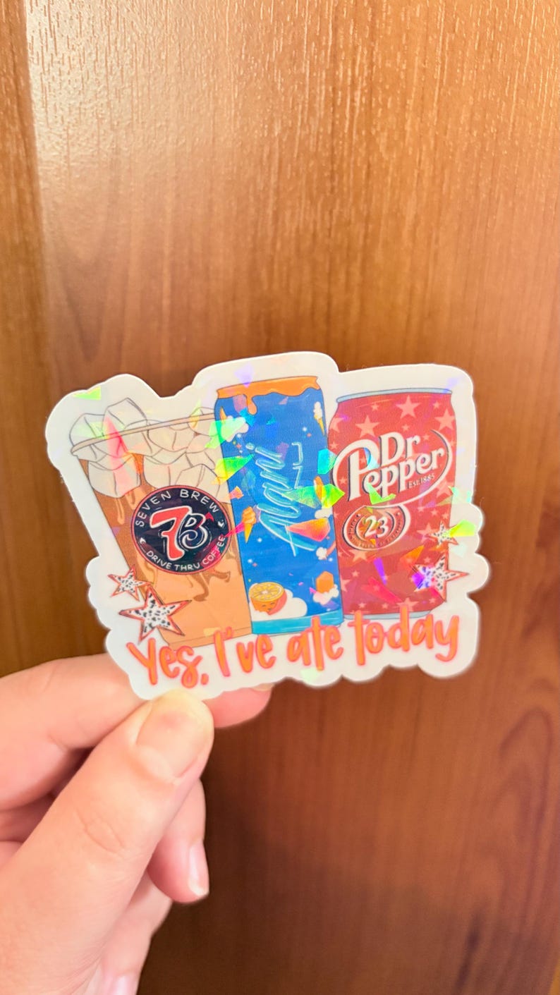 May include: A holographic sticker featuring three beverage containers: a Seven Brew iced coffee cup, a blue Alani Nu energy drink can, and a red Dr. Pepper can. The sticker includes orange text at the bottom that reads, Yes, I've ale today.