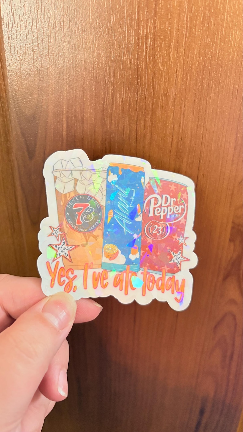 May include: A holographic sticker featuring three beverage containers: a Seven Brew coffee cup, a blue Alani Nu energy drink can, and a red Dr. Pepper can. The sticker includes the text "Yes, I've ate today" and decorative star shapes.