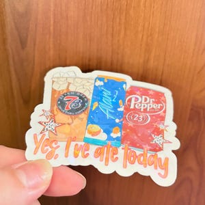 May include: A die-cut sticker featuring illustrations of a 7 Brew coffee cup, a blue Alani Nu energy drink can, and a Dr. Pepper soda can. The sticker includes the orange text "Yes, I've ate today" and decorative star accents on a white background.