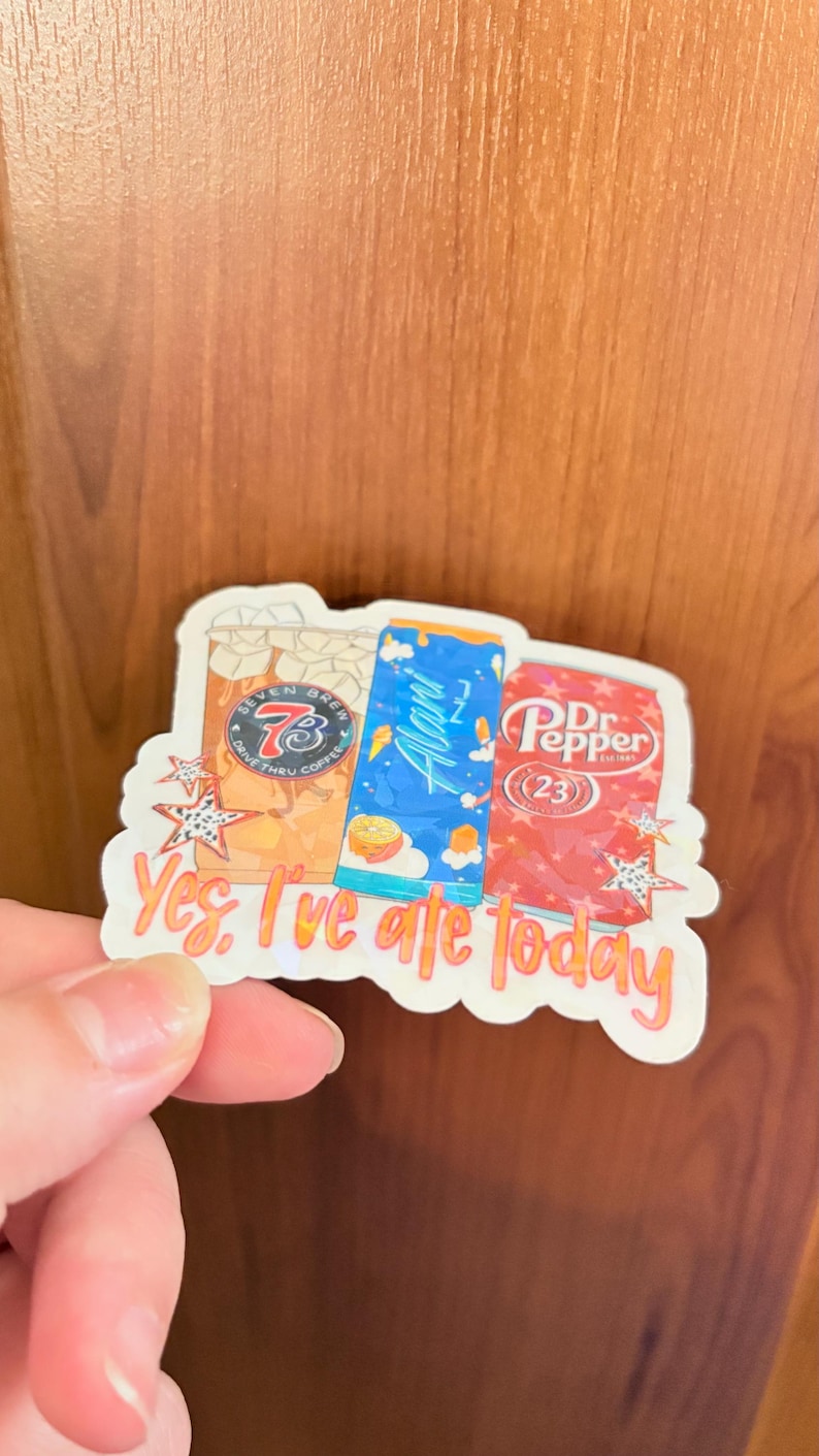 May include: A die-cut sticker featuring illustrations of a 7 Brew coffee cup, a blue Alani Nu energy drink can, and a Dr. Pepper soda can. The sticker includes the orange text "Yes, I've ate today" and decorative star accents on a white background.
