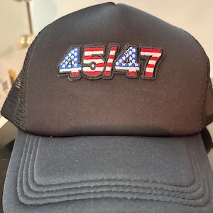 May include: Black trucker hat with the number "45/47" embroidered on the front in red, white, and blue. The hat has a mesh back and a curved brim. A casual accessory.