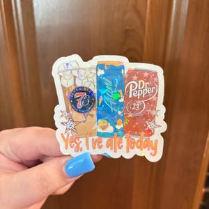 May include: A holographic sticker featuring a Seven Brew iced coffee, an Alani Nu energy drink, and a Dr. Pepper can. The design includes small star shapes and the orange text "Yes, I've ate today" printed at the bottom of the sticker.