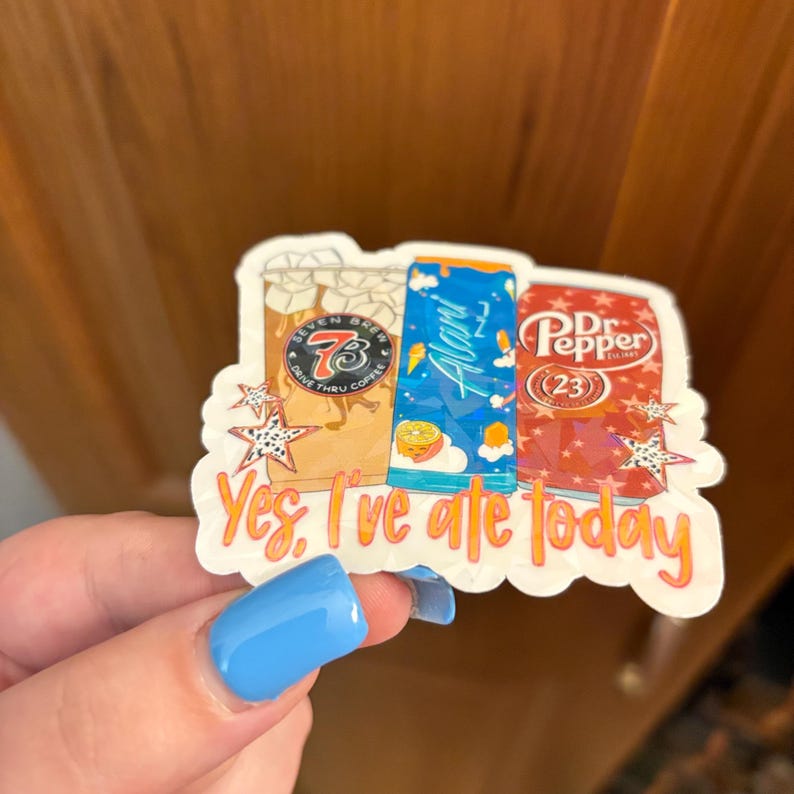 May include: A die-cut sticker featuring illustrations of a Seven Brew coffee cup, a blue Alani Nu energy drink can, and a red Dr. Pepper can. The sticker includes the orange text "Yes, I've ate today" at the bottom and decorative star accents.