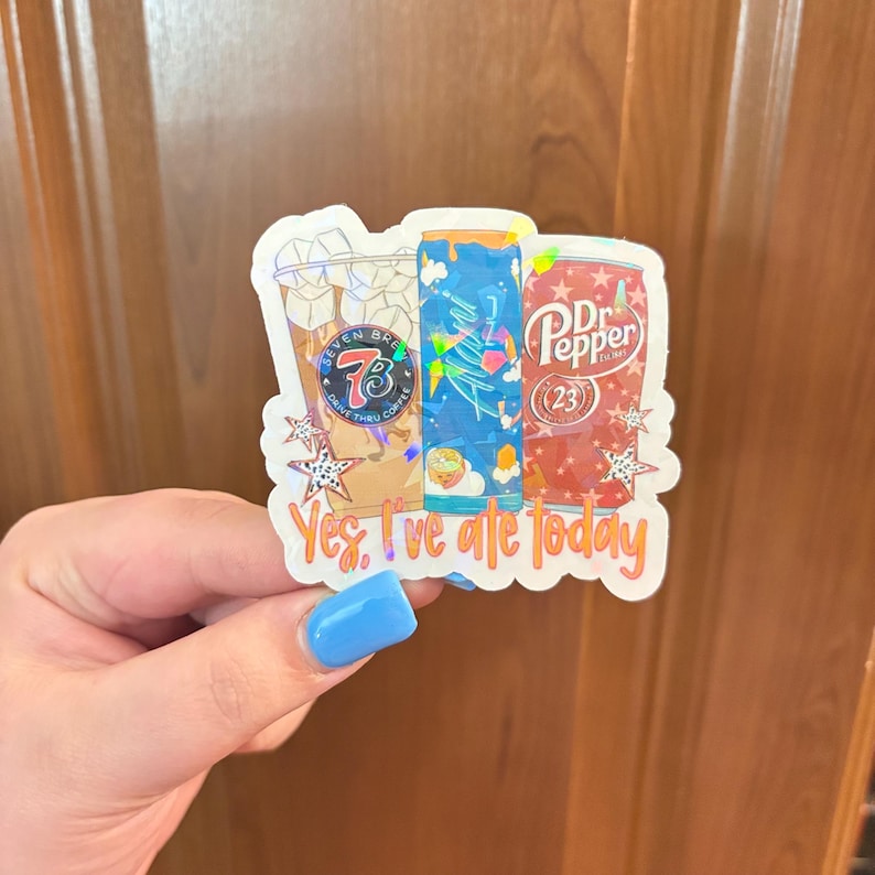 May include: A die-cut sticker featuring three beverage containers: a Seven Brew iced coffee cup, a blue energy drink can, and a red Dr. Pepper can. The design includes holographic star accents and the orange text "Yes, I've ate today" at the bottom.