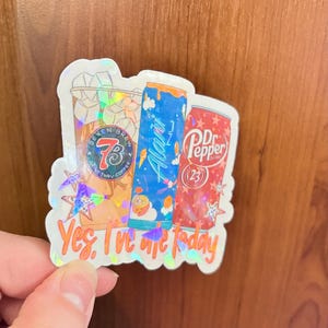 May include: A holographic sticker featuring a Seven Brew coffee cup, a blue Alani Nu energy drink can, and a red Dr. Pepper can. The sticker includes the text "Yes, I've ate today" in orange script at the bottom, accented with small holographic stars.